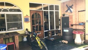 A building with a wooden exterior, a large window, and a door. There is a bicycle parked outside and a trash can nearby. - ANKES Hostel (Hengchun)
