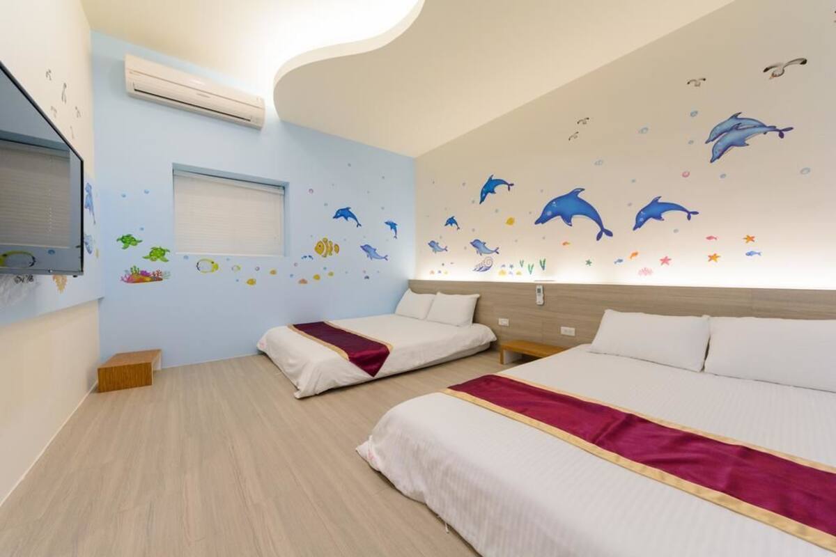 Habitación de hotel con dos camas, un televisor y una pared decorada con motivos marinos.