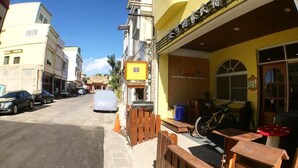 A street view with a yellow building featuring a signboard, wooden fences, and parked bicycles. - ANKES Hostel (Hengchun)