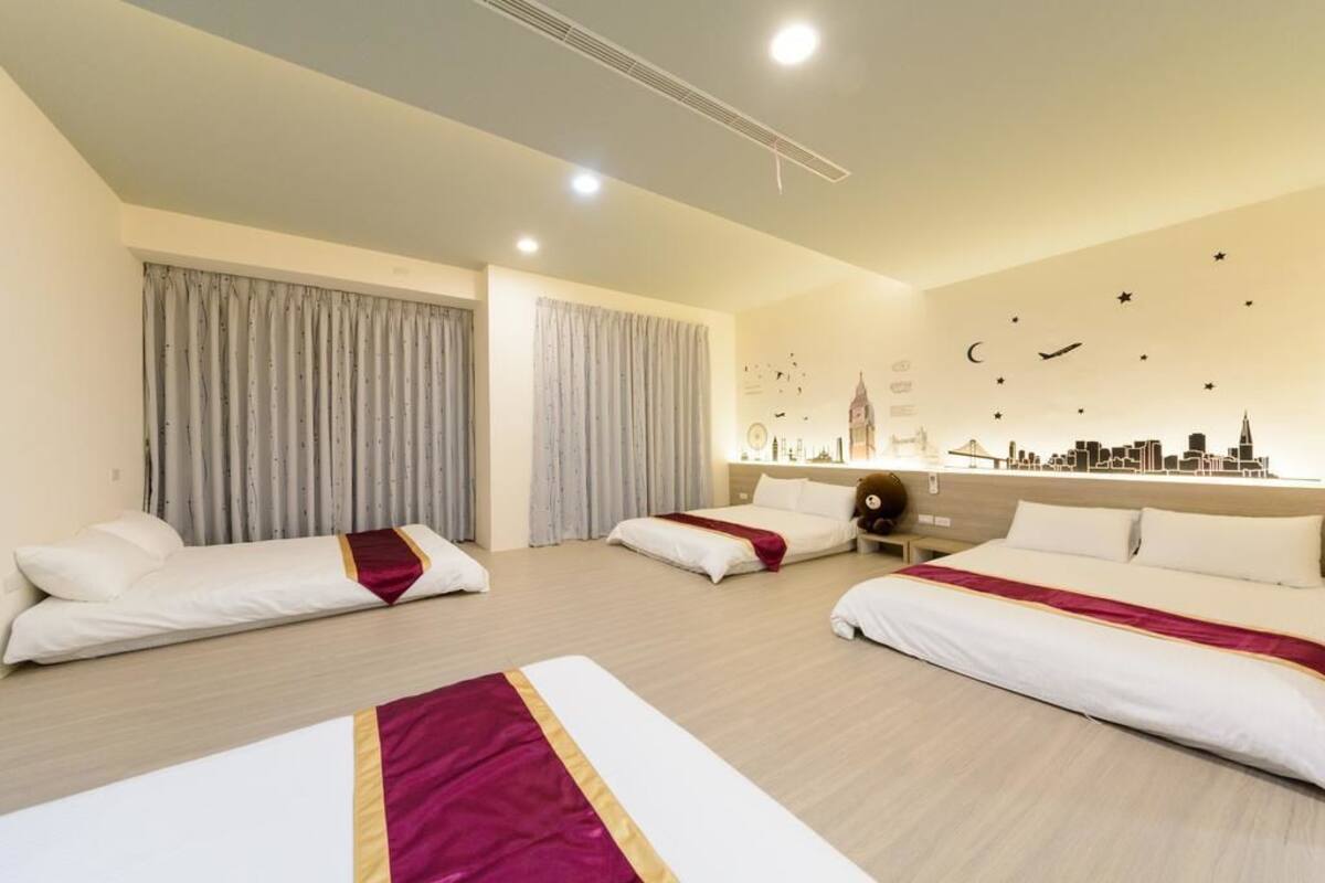 Habitación de hotel con tres camas, un mural del horizonte urbano y un diseño del cielo nocturno en la pared.