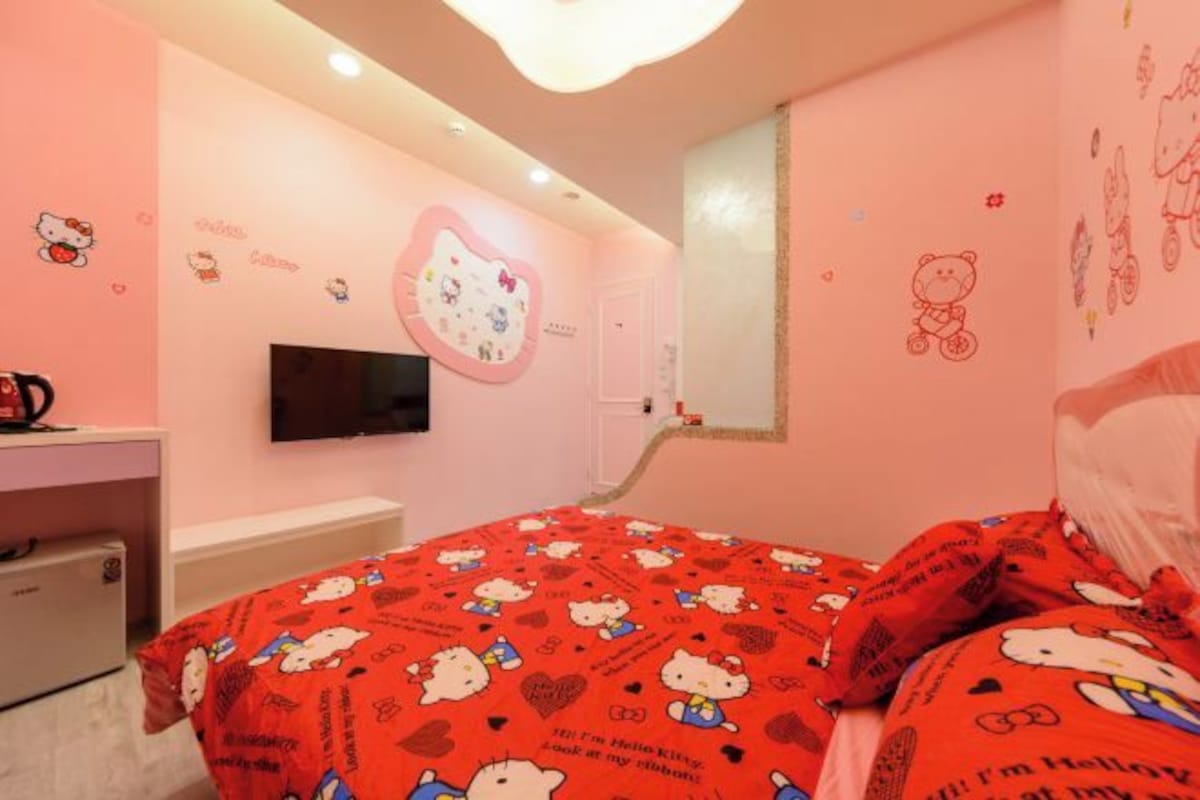 A pink-themed room with a bed, a TV, and a desk.