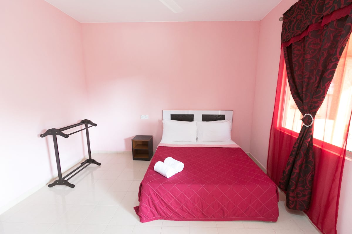 A neatly made bed with a red bedspread, a black metal rack, and a small wooden nightstand.