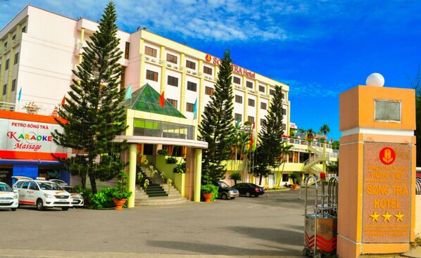 A hotel with a prominent sign, a parking area, and a building with a green roof.