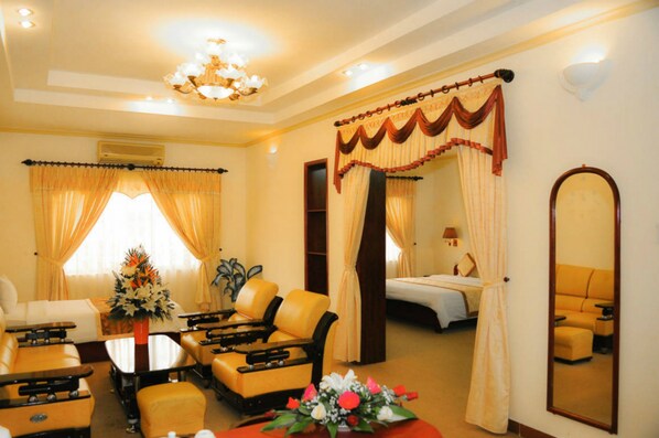 A hotel room with a bed, a sitting area with a sofa and chairs, a dining table, and a large mirror. - Song Tra Hotel (Nghia Lo)