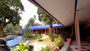 Un espace extérieur abrité, avec une voiture garée devant, entouré de verdure et bordé d’un bâtiment dont le toit est bleu.