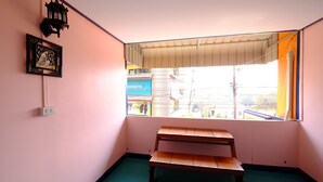 Une pièce comprenant un banc, un luminaire fixé au mur, un tableau encadré et une fenêtre donnant sur des bâtiments à l’extérieur.