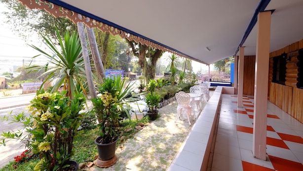Un espace extérieur abrité, agrémenté de plantes en pot, de chaises blanches et d’un sol à carreaux.