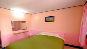 Une chambre avec une couvre-lit verte, une petite table de chevet, un miroir et un tableau accroché au mur.