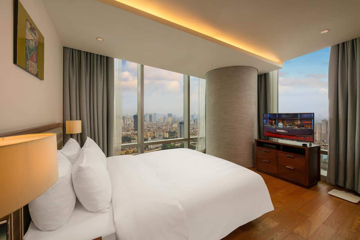 Une chambre d’hôtel avec un grand lit, une télévision et une vue sur la ville, grâce à de grandes fenêtres.