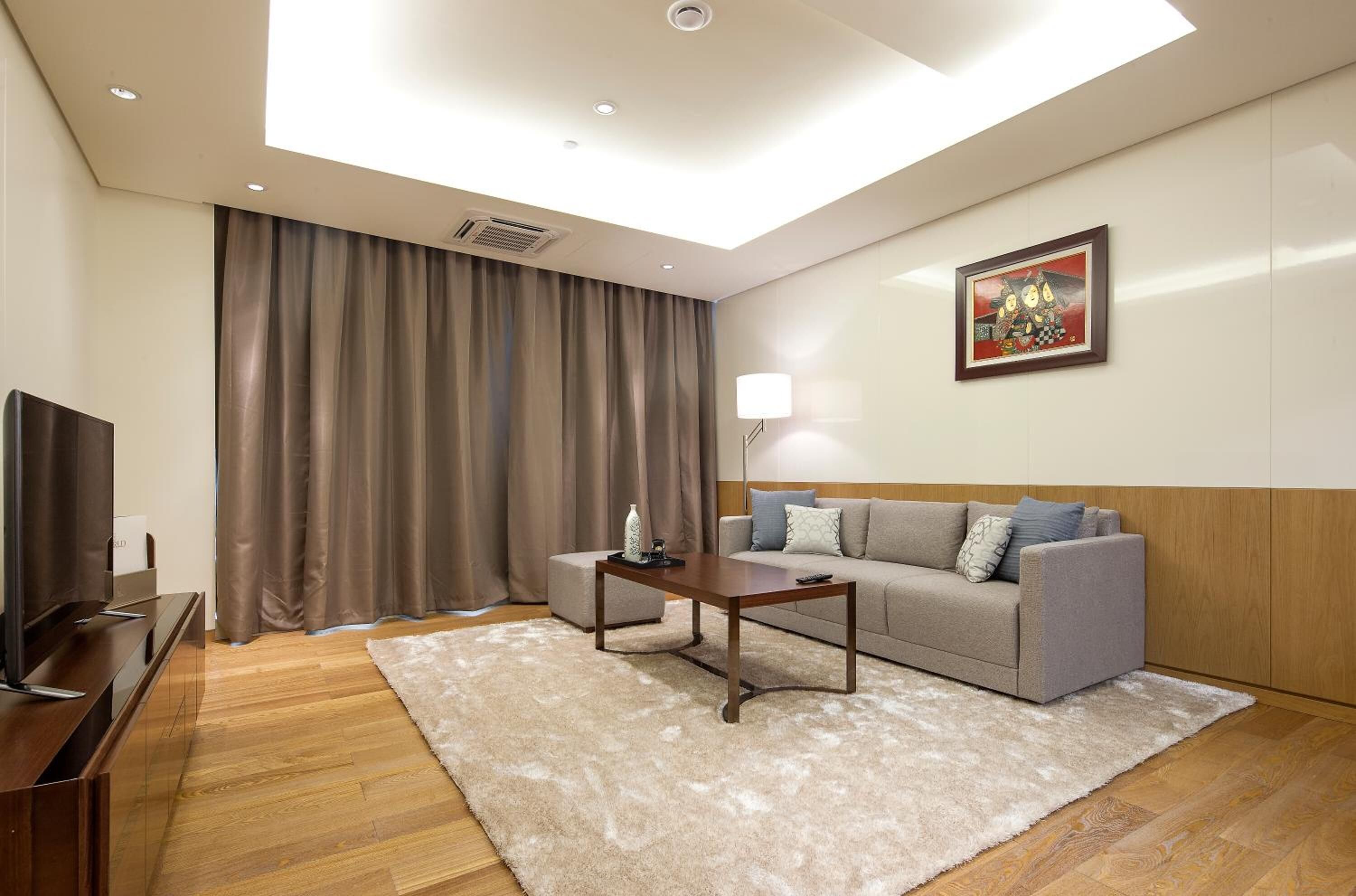 A modern living room with a flat-screen TV, a sofa, a coffee table, and a large window with curtains.
