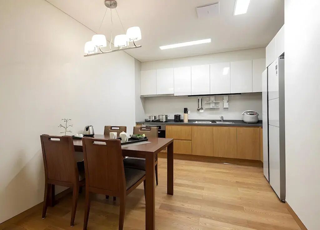 A compact kitchen with white cabinets, a wooden dining table, and a built-in oven.