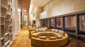 A spacious lobby with a curved seating area, a long hallway with shelves, and large windows offering a city view. - Lotte The Residence (Hanoi)