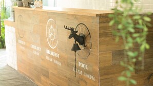 A reception desk with a wooden finish and a clock indicating check-in, check-out, breakfast, and pool hours. - Ginger Bread House - Pet Lover Resort (Nakhon Nayok)