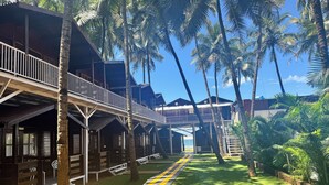 A resort with wooden buildings, a covered walkway, and a well-maintained lawn. - Agonda Paradise (Canacona)