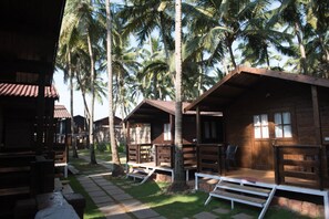 A row of wooden cabins with a paved walkway between them, surrounded by palm trees. - Agonda Paradise (Canacona)
