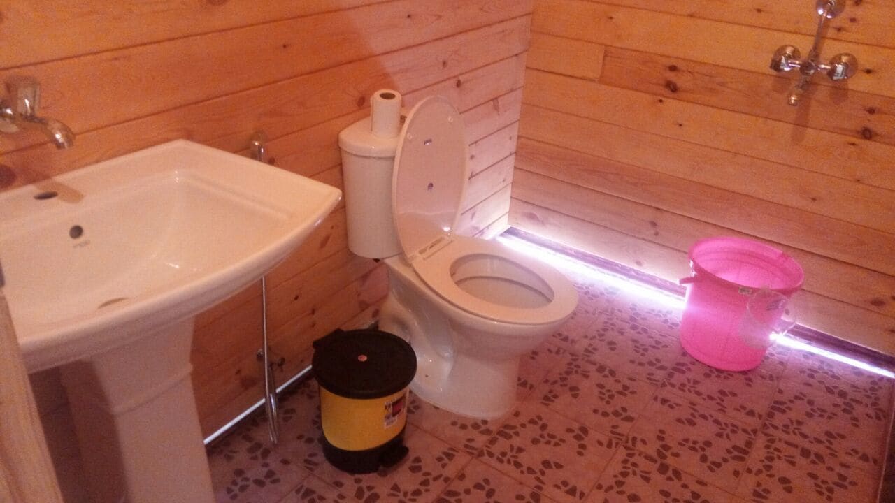 Un baño con paneles de madera, un lavamanos blanco, un inodoro y un cubo rosa.