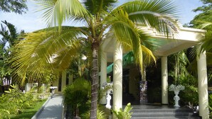 A covered entrance with palm trees, a statue, and a staircase leading to a building. - Tropicana Beach Villa at  VIP Resort (Rayong)