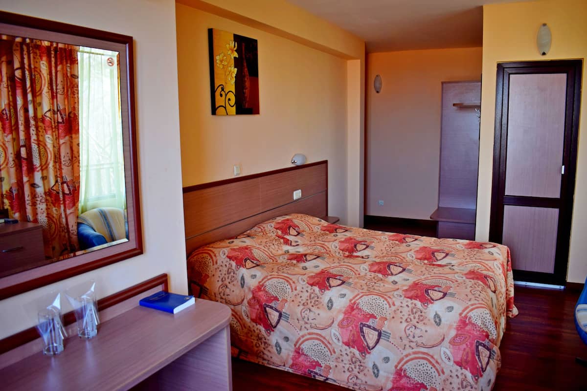 A hotel room with a bed, a desk with a mirror, a painting on the wall, and a door.