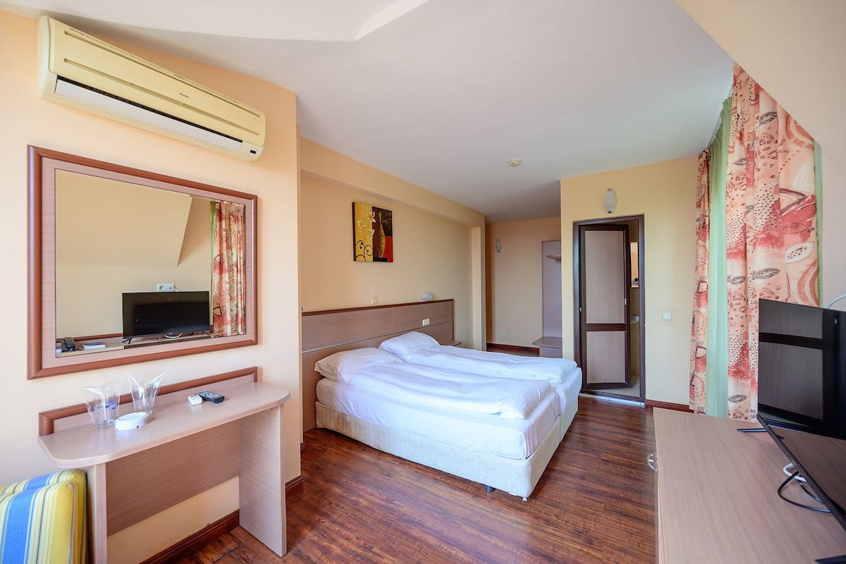 A hotel room with a bed, a desk with a mirror, a television, and a wardrobe.