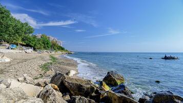 A rocky beach with a clear view of the sea and a building in the background.