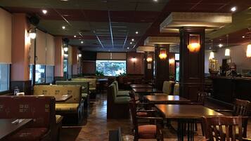 A restaurant with booths and tables, a bar area, and a large window with a view of trees.
