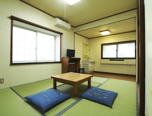 Een traditionele Japanse kamer met tatami matten, een houten tafel, een televisie en een kleine kitchenette.