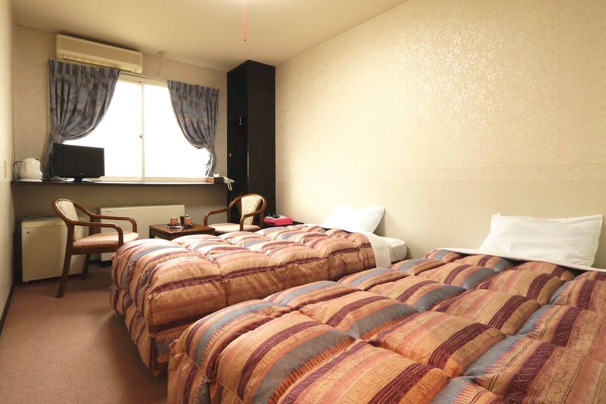 A hotel room with two beds, a desk with a computer, a chair, and a window with curtains.