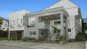 A modern building with a sign reading "Service Tanne." It features a prominent staircase, large windows, and potted plants around the entrance. - Hakuba Tsugaike Sunrise TANNE (Otari)
