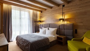 Une chambre à coucher avec un grand lit, des poutres apparentes en bois au plafond, un fauteuil vert et une table de chevet.