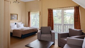 Une chambre d’hôtel avec un lit, deux fauteuils, une petite table et un balcon avec des rideaux.