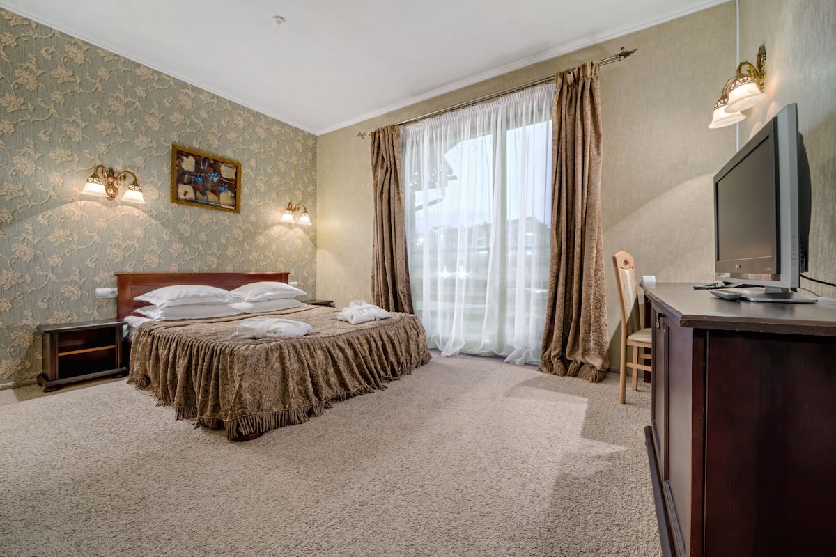 A hotel room with a large bed, a desk with a TV, and a window with curtains.