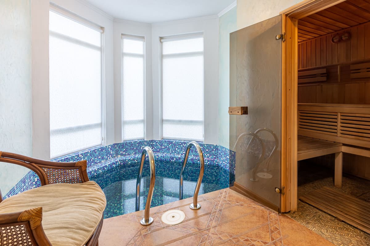 A spa area with a glass-enclosed hot tub, wooden sauna benches, and a seating area with a cushioned chair.