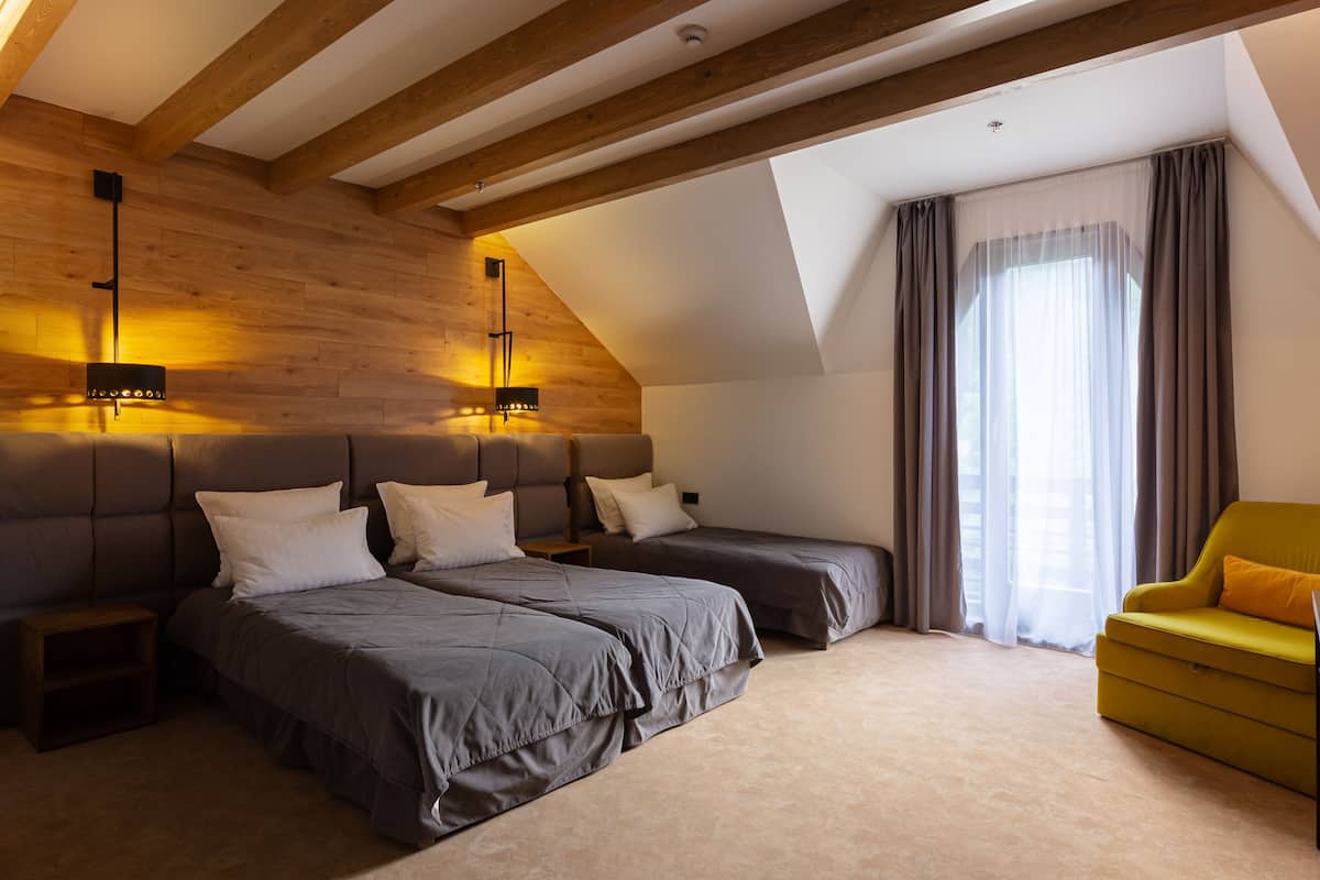 A modern bedroom with two beds, a sofa, and a large window with curtains.