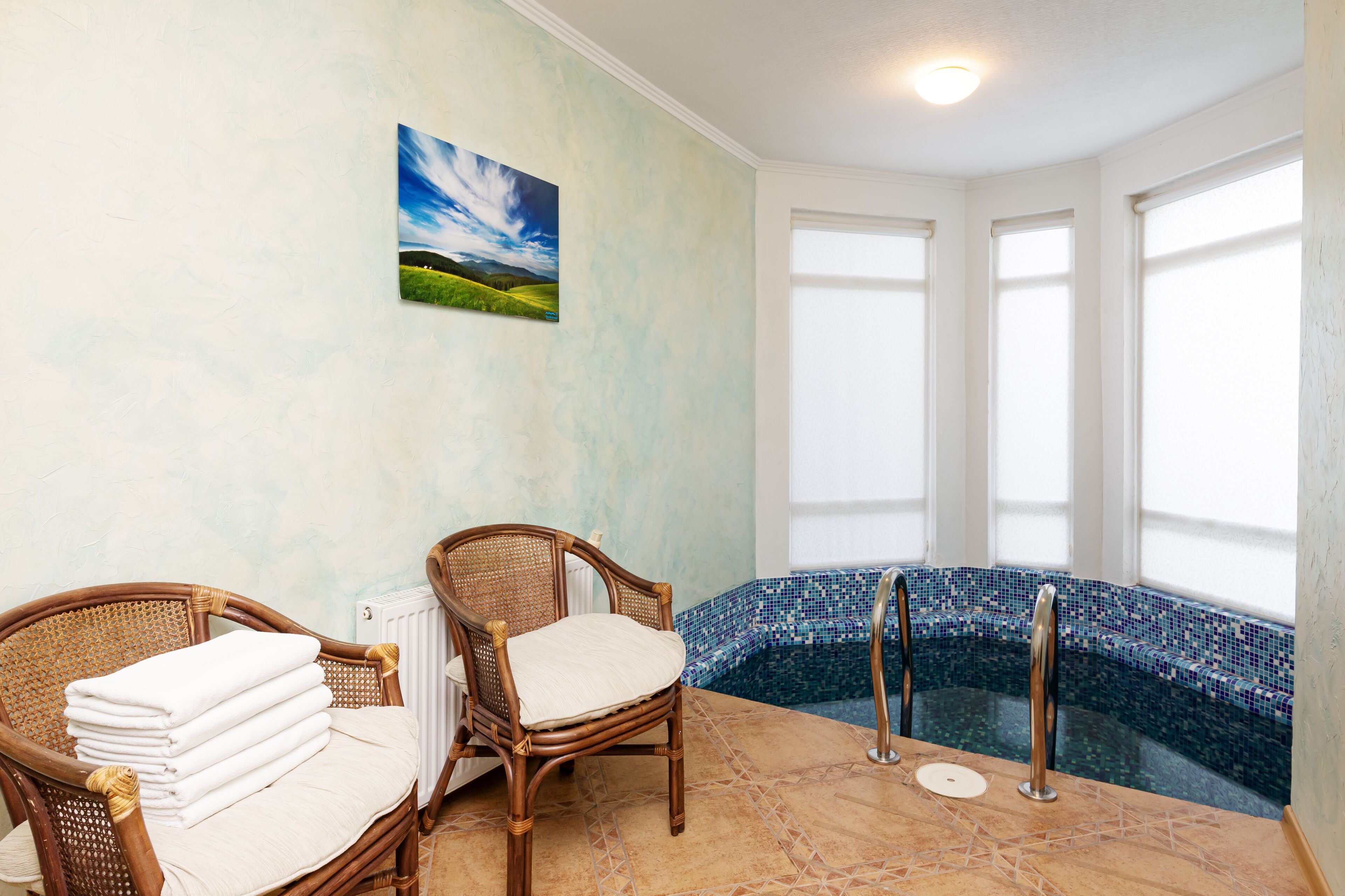 A spa area with a mosaic-tiled hot tub, wicker chairs, and a painting of a landscape.