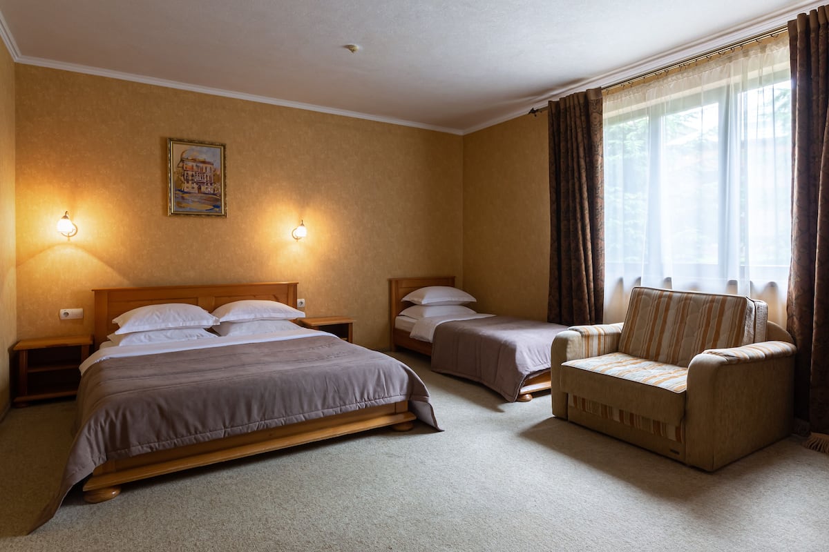 A hotel room with two beds, a sofa, and a chair. There are two wall-mounted lamps and a painting on the wall.