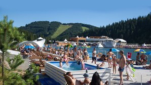 Un complexe hôtelier situé en bord de mer, doté d’une piscine, de chaises longues et offrant une vue sur l’eau et les collines.