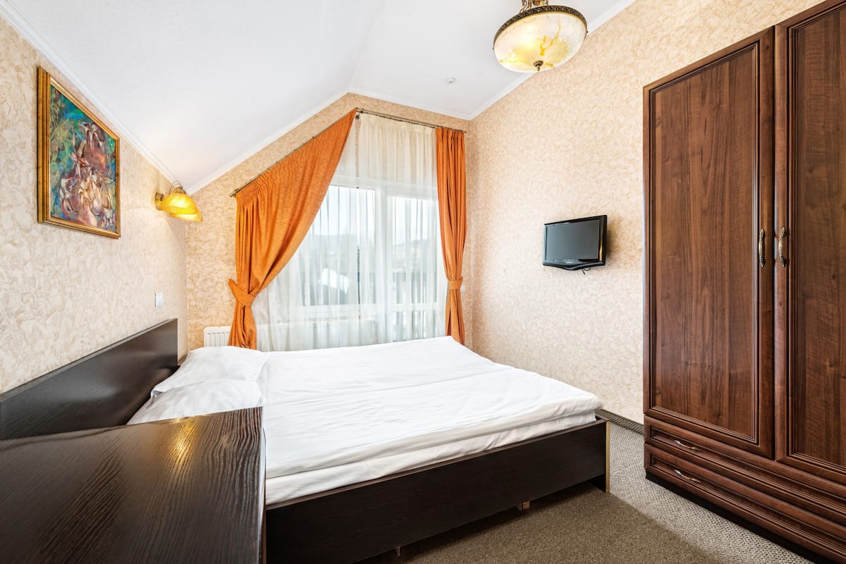 A bedroom with a bed, a wardrobe, a painting, a television, and a window with curtains.