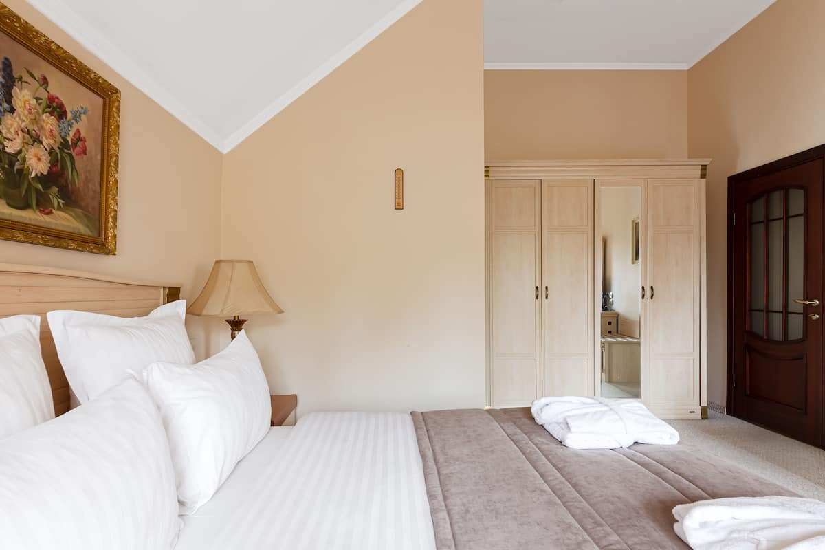 A hotel room with a large bed, a wardrobe, and a painting on the wall.