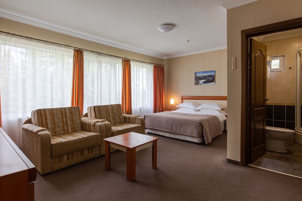 A hotel room with a bed, two armchairs, a small table, and a bathroom visible through an open door.