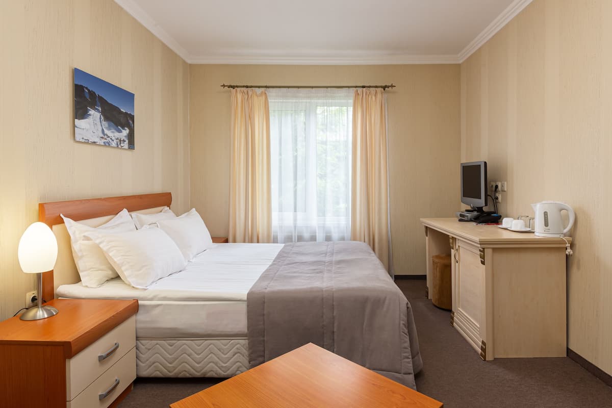 A hotel room with a bed, bedside table, desk, and a television.