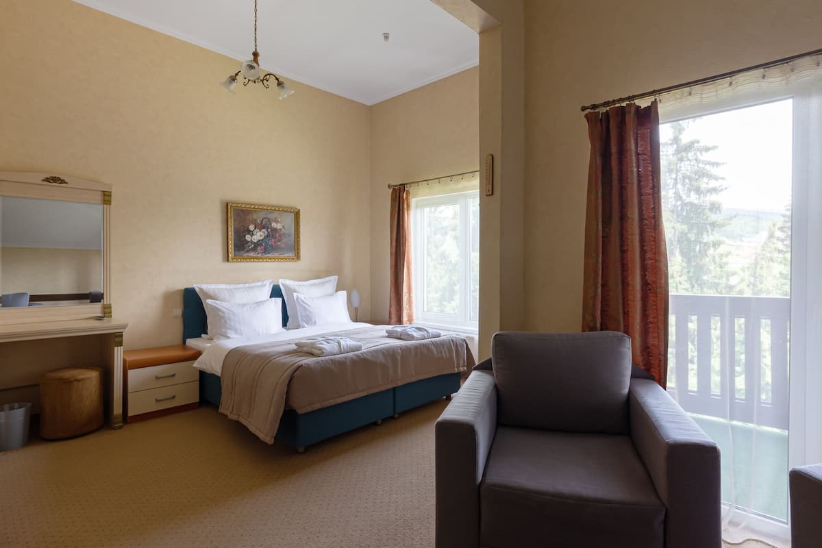 A hotel room with a bed, a sofa, a desk, a chair, a window with curtains, and a painting on the wall.