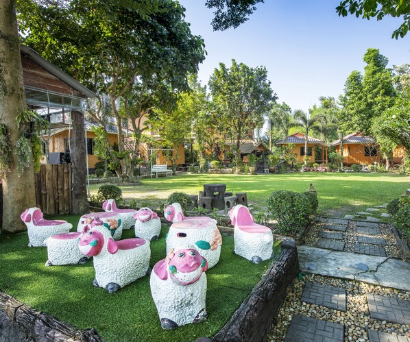 Um jardim com esculturas de ovelhas artificiais, cerca de madeira e um caminho pavimentado.