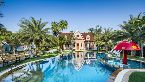 A swimming pool with a reflection of palm trees and a building with a red roof. - Greenview Resort (Nakhon Nayok)