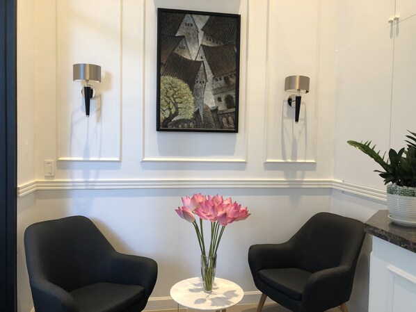 Una habitación moderna con dos sillas negras, una mesita redonda con un jarrón de flores rosas y una obra de arte enmarcada en la pared.