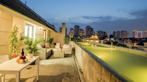 A rooftop terrace with a dining table, seating, and a view of the city skyline at dusk. - La Cigale Residence (Ho Chi Minh City)