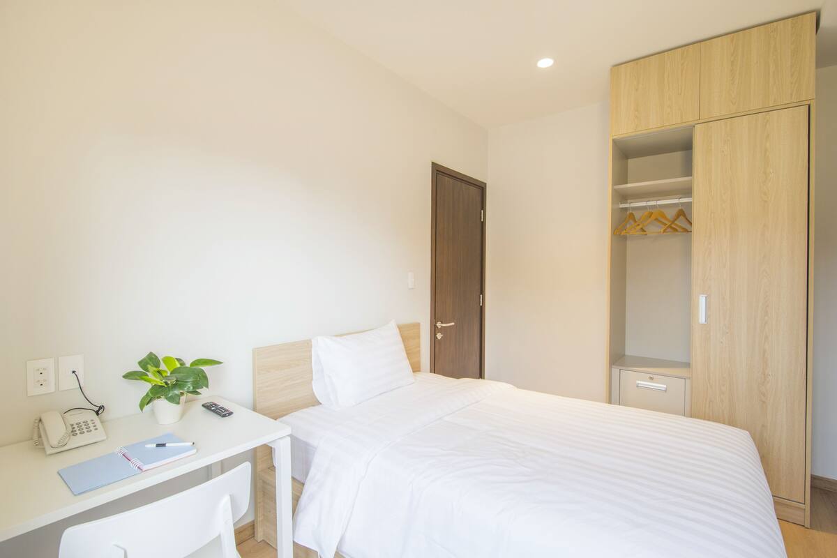A bedroom with a bed, a desk with a plant, a phone, and a hanging closet.