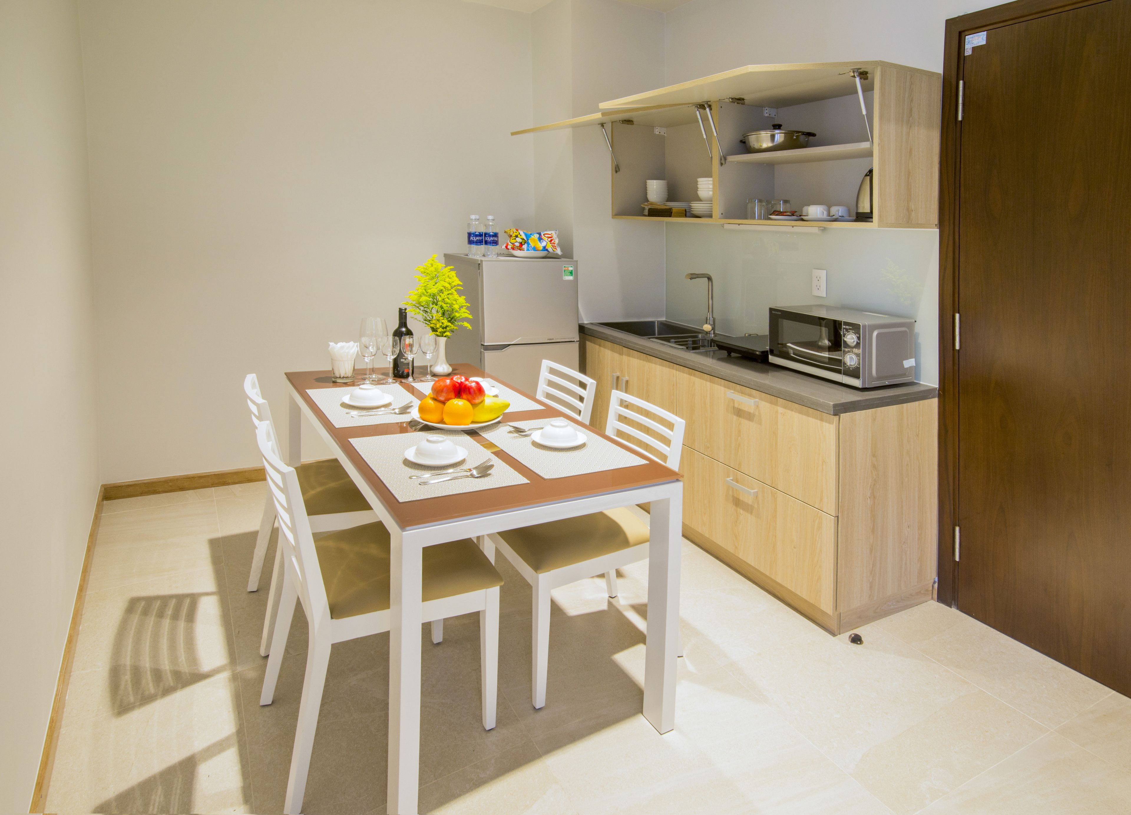A compact kitchen with a dining area, including a table set with plates, a bowl of fruit, and a vase with flowers.