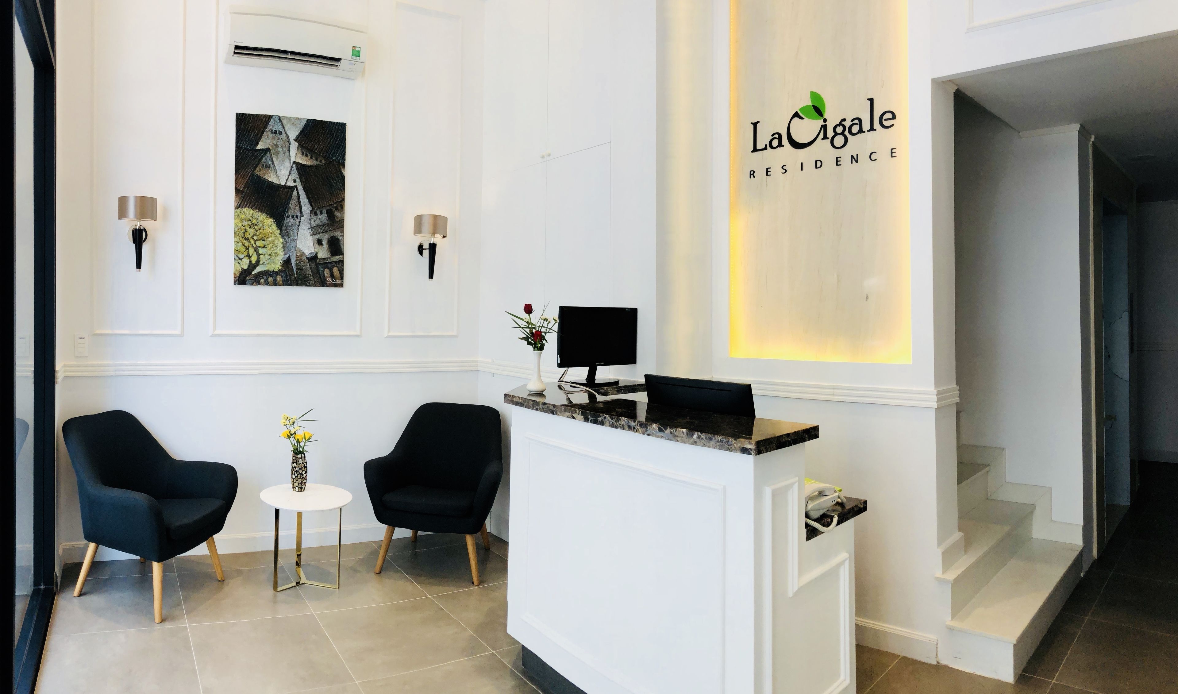 A reception area with a desk, two chairs, a small table with a vase, and a wall-mounted sign.