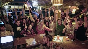 Eine Gruppe von Menschen in einer Bar mit rustikalem Ambiente, darunter freiliegende Holzbalken und Pendelleuchten.