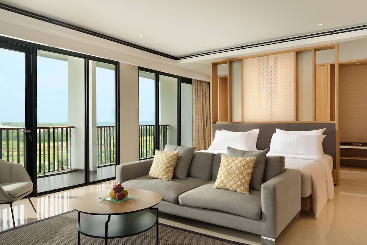 Een moderne hotelkamer met een ruim balkon, een bank met gestreepte kussens, een ronde salontafel en een keurig opgemaakt bed.